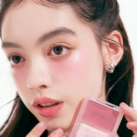 Glow blush balm compact held near face, pink blush balm inside square tray for cheeks.