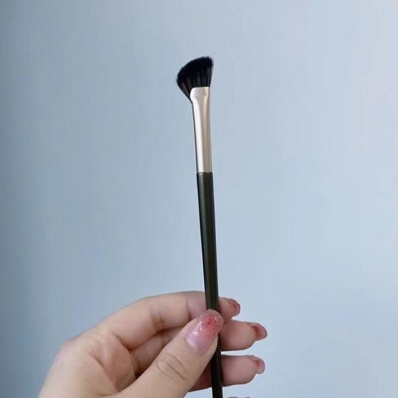 Fan nose shadow brush held in hand; green handle, black bristles, gold ferrule.