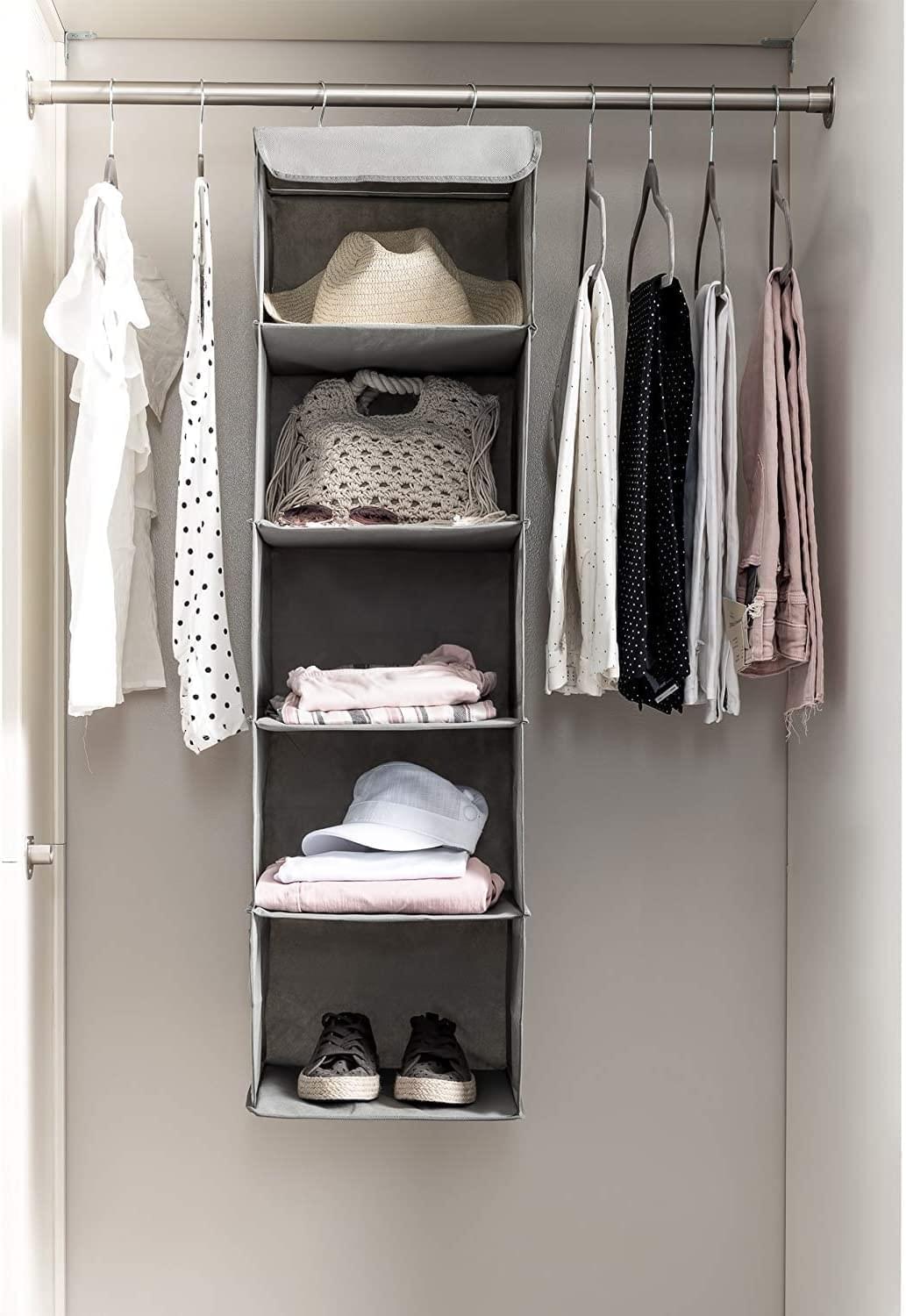 Hanging closet organizer shelf unit with grey fabric compartments for shirts and folded items.