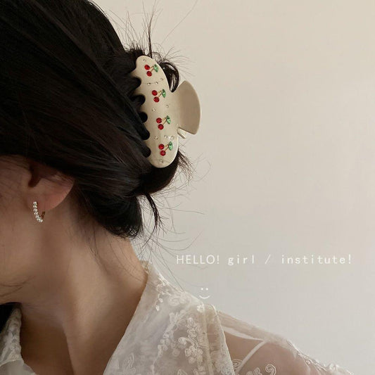 Cream rhinestone cherry hair claw clip clipped in dark hair, side view