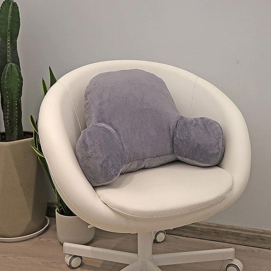 Dark grey reading pillow backrest sitting on a cream lounge chair