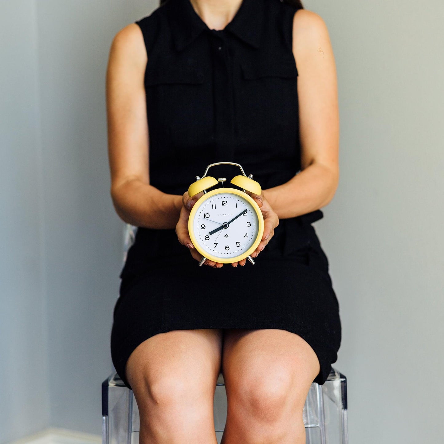 Yellow alarm clock held in hands, white dial with twin bells
