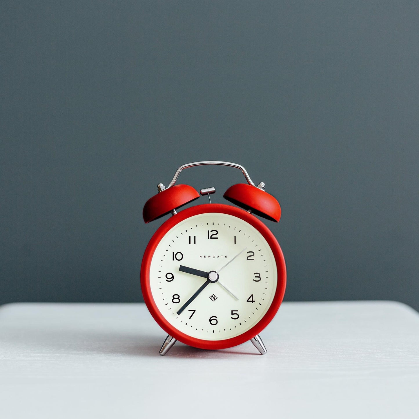 Red alarm clock with twin bells and white dial on a table