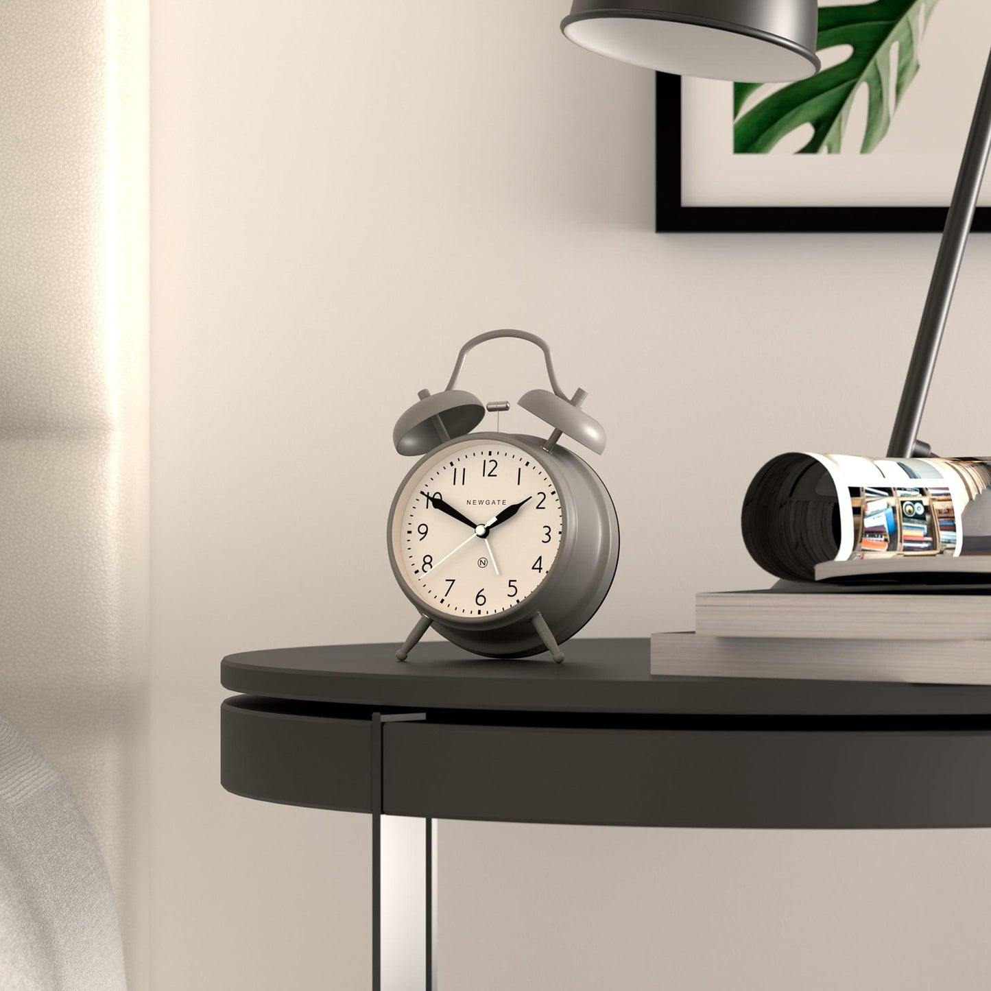 Grey twin-bell alarm clock on a bedside table with white dial and black hands