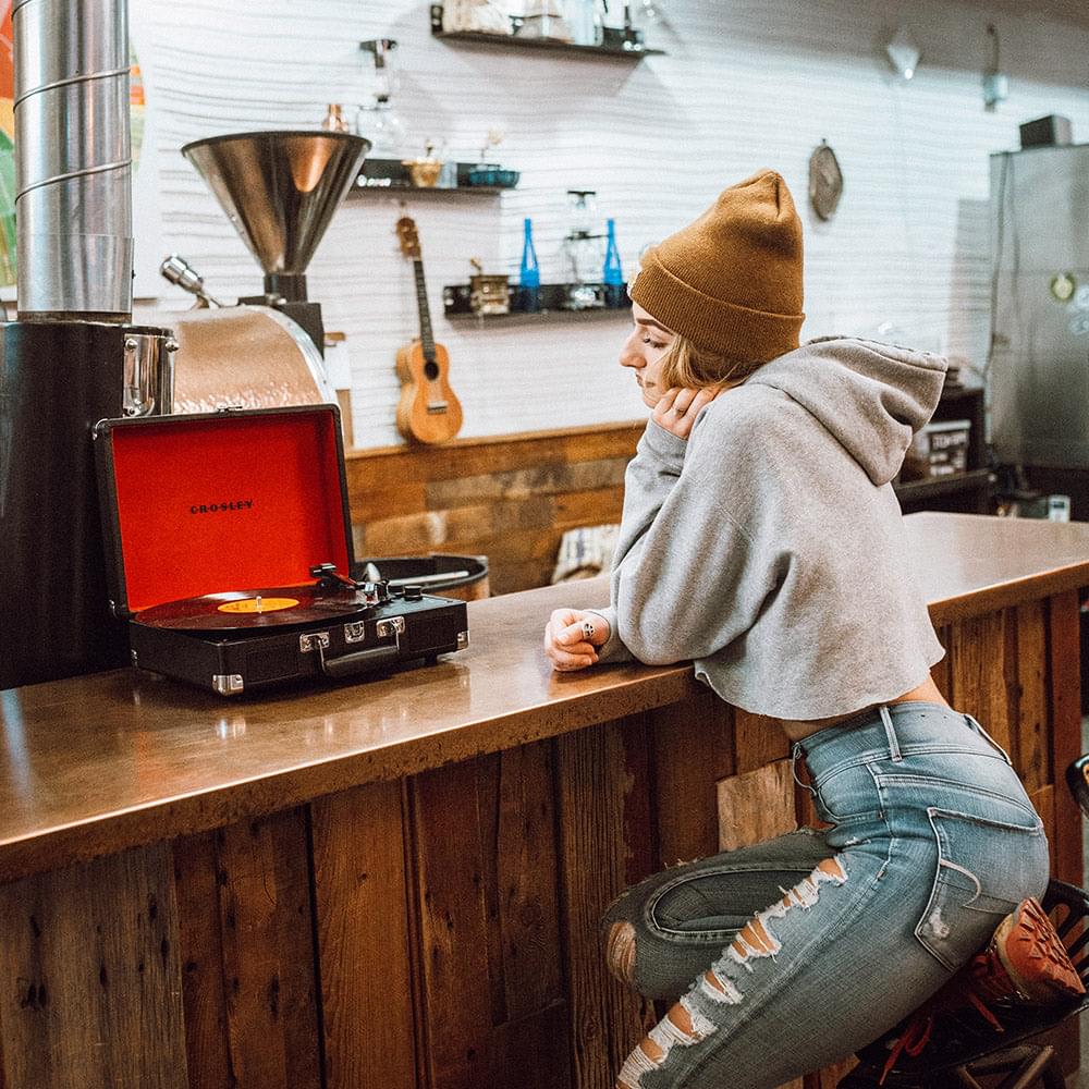 Portable turntable with open black case and red lid beside a person at a counter