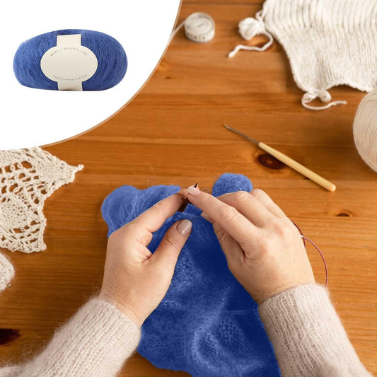 Blue yarn ball while crocheting; hands hold yarn and hook on wooden table