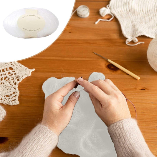 White yarn ball and skein on wooden table with yarn strands and crochet piece