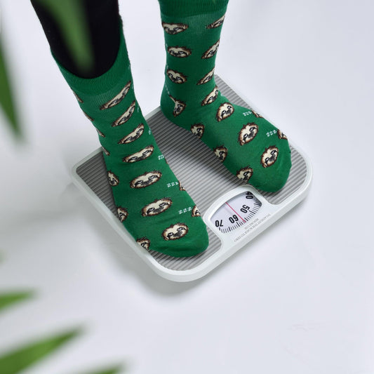 Bathroom scale with ridged platform and analog dial, feet in green patterned socks