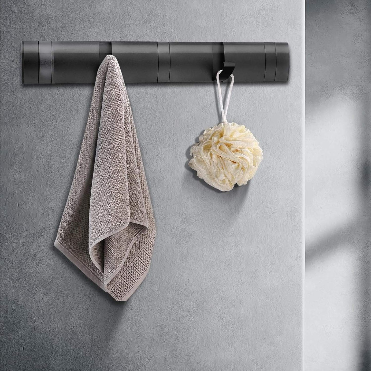 Black coat rack wall mount with retractable hooks holding a towel and loofah