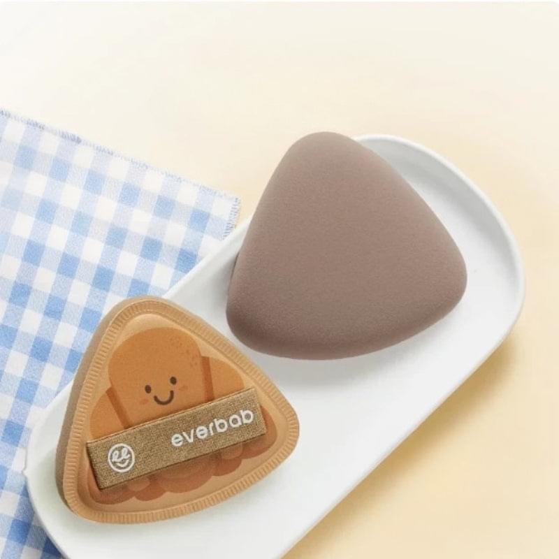 Beige triangle makeup sponge puff in a tray with a matching pouch