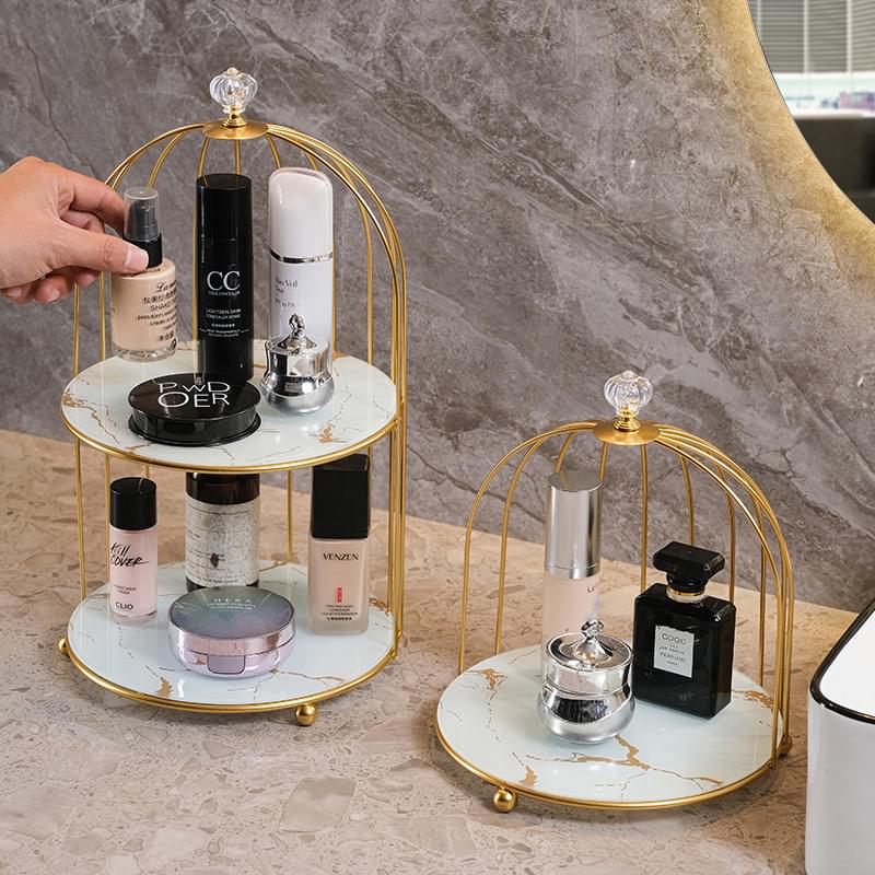 Two-tier gold birdcage cosmetic organizer with white marble trays holding skincare bottles