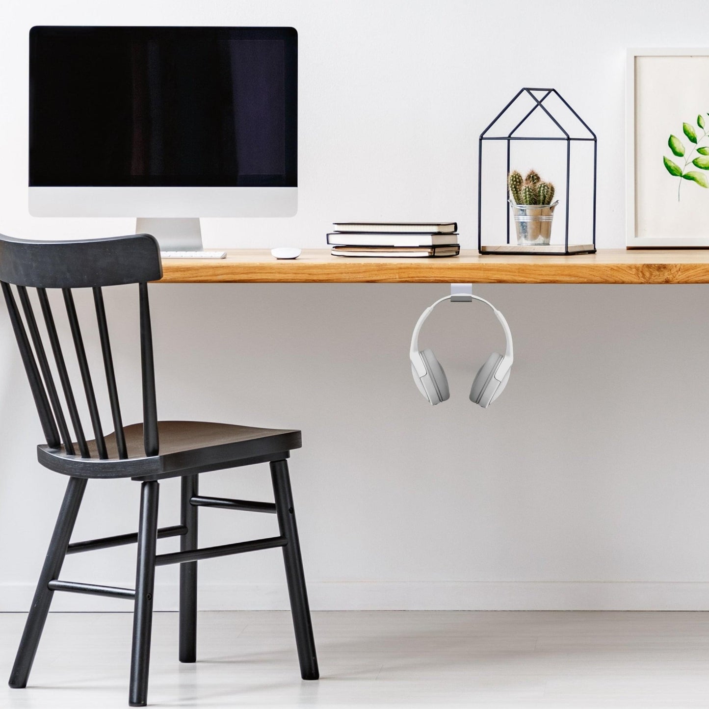 Under-desk headphone hook with white headphones hanging below the desk
