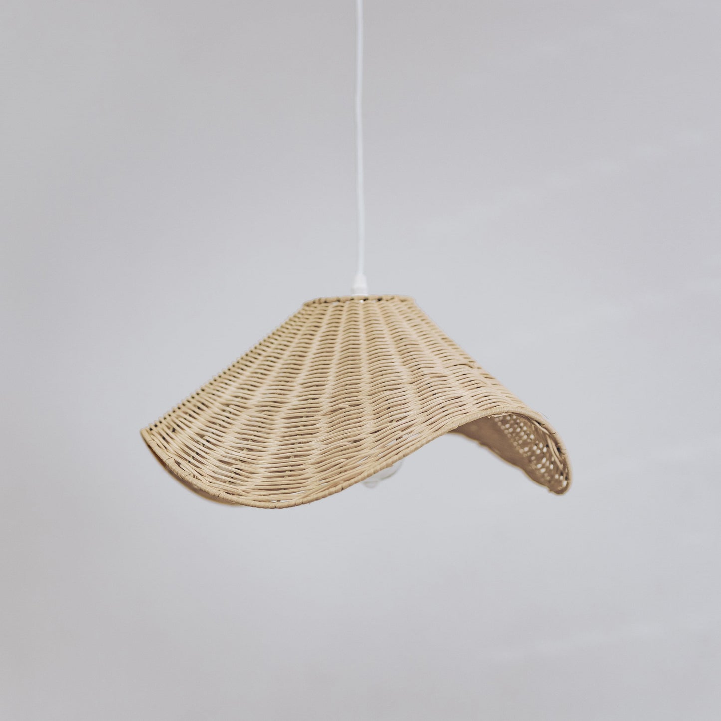 Wavy rattan pendant light shade with curved opening, hanging from white cord