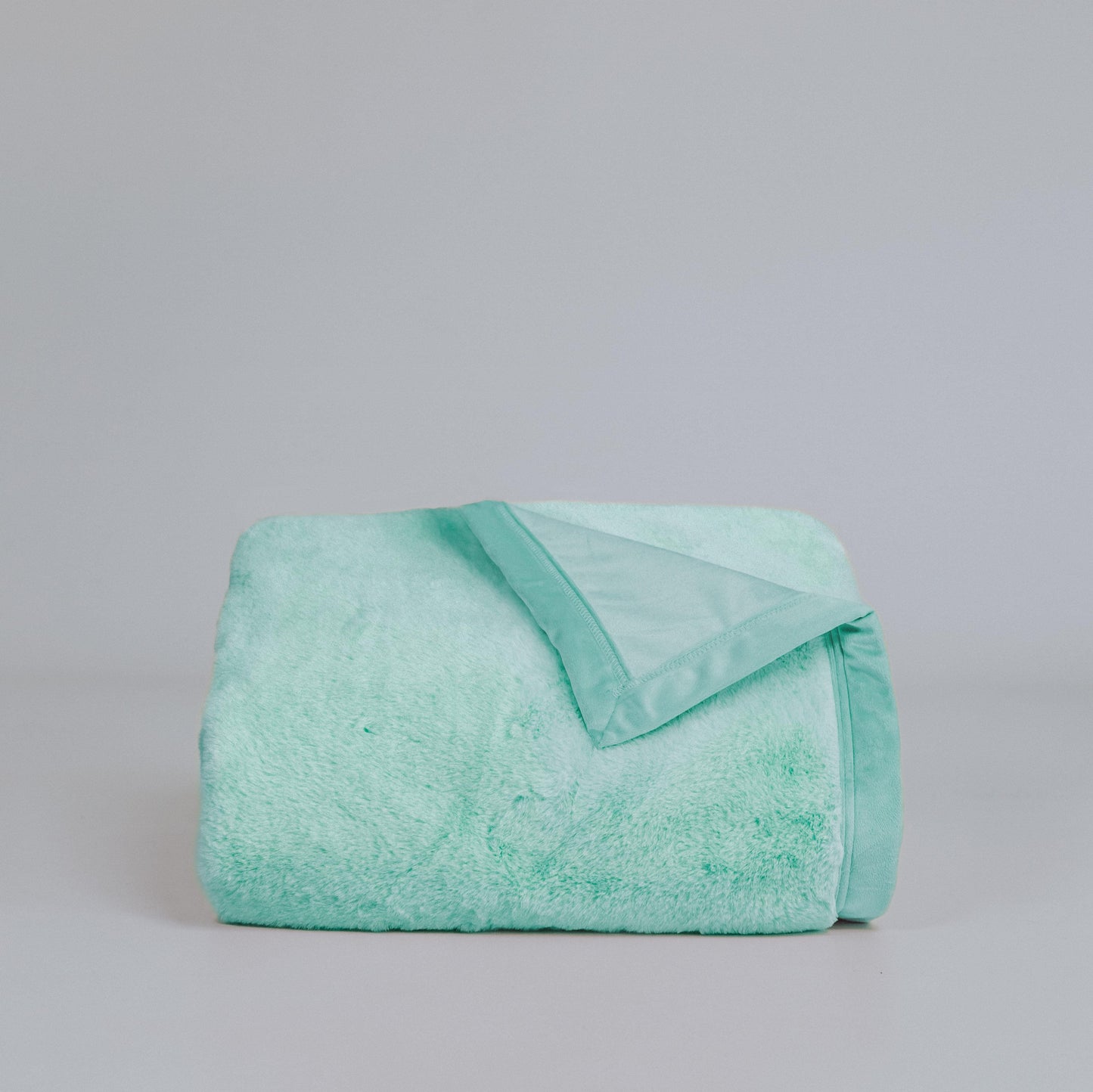 Turquoise plush fur throw blanket, neatly folded with visible folded edge detail.
