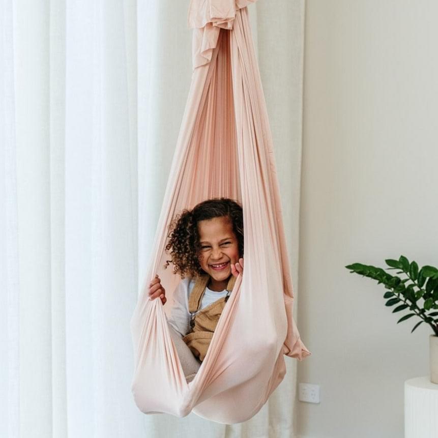 Soft pink fabric swing cocoon with open hammock pouch and ruffled top, child seated.