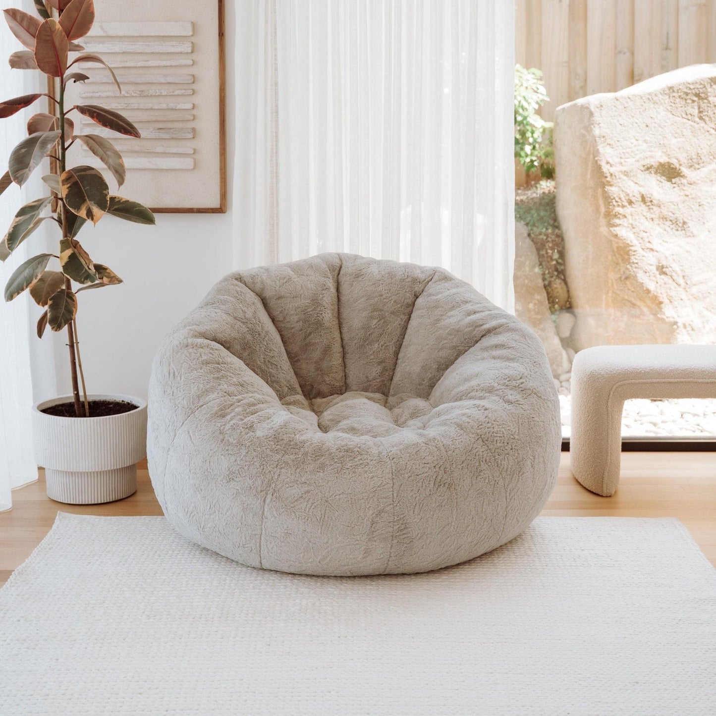 Round plush nest lounger in light beige, on rug near window