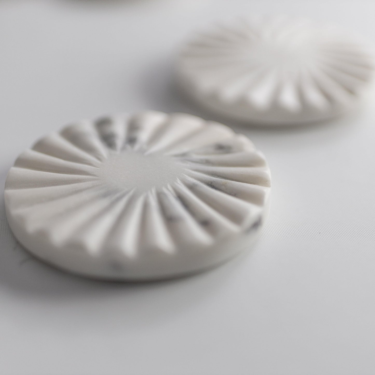 Close-up of a white scalloped marble coaster with raised radial ridges