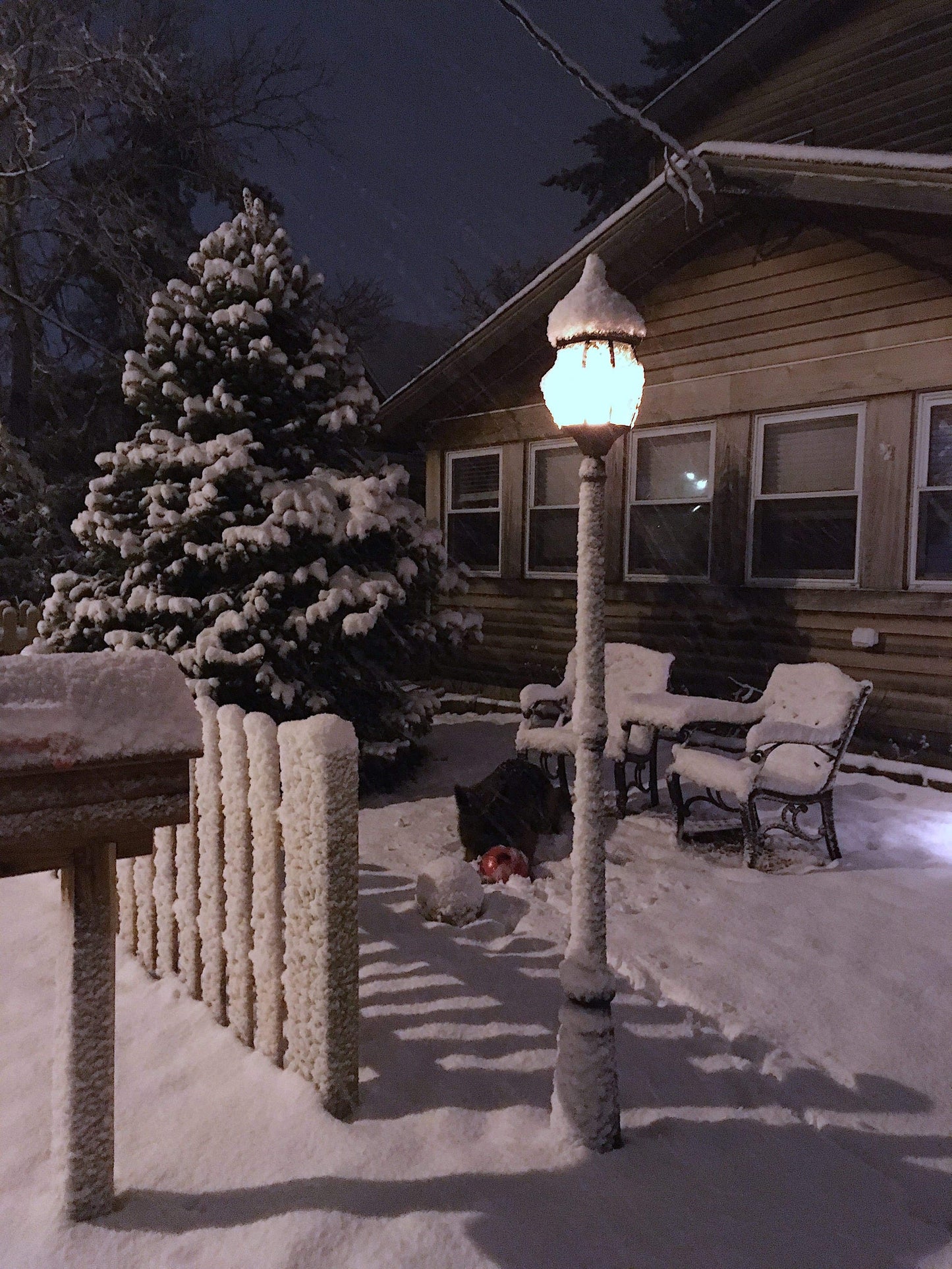 Black outdoor lamp post with lit lantern shade and frosted snow on surroundings.