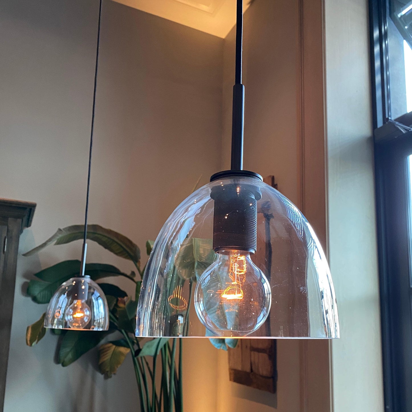 Black pendant light with clear bell glass shade and visible warm bulb inside.