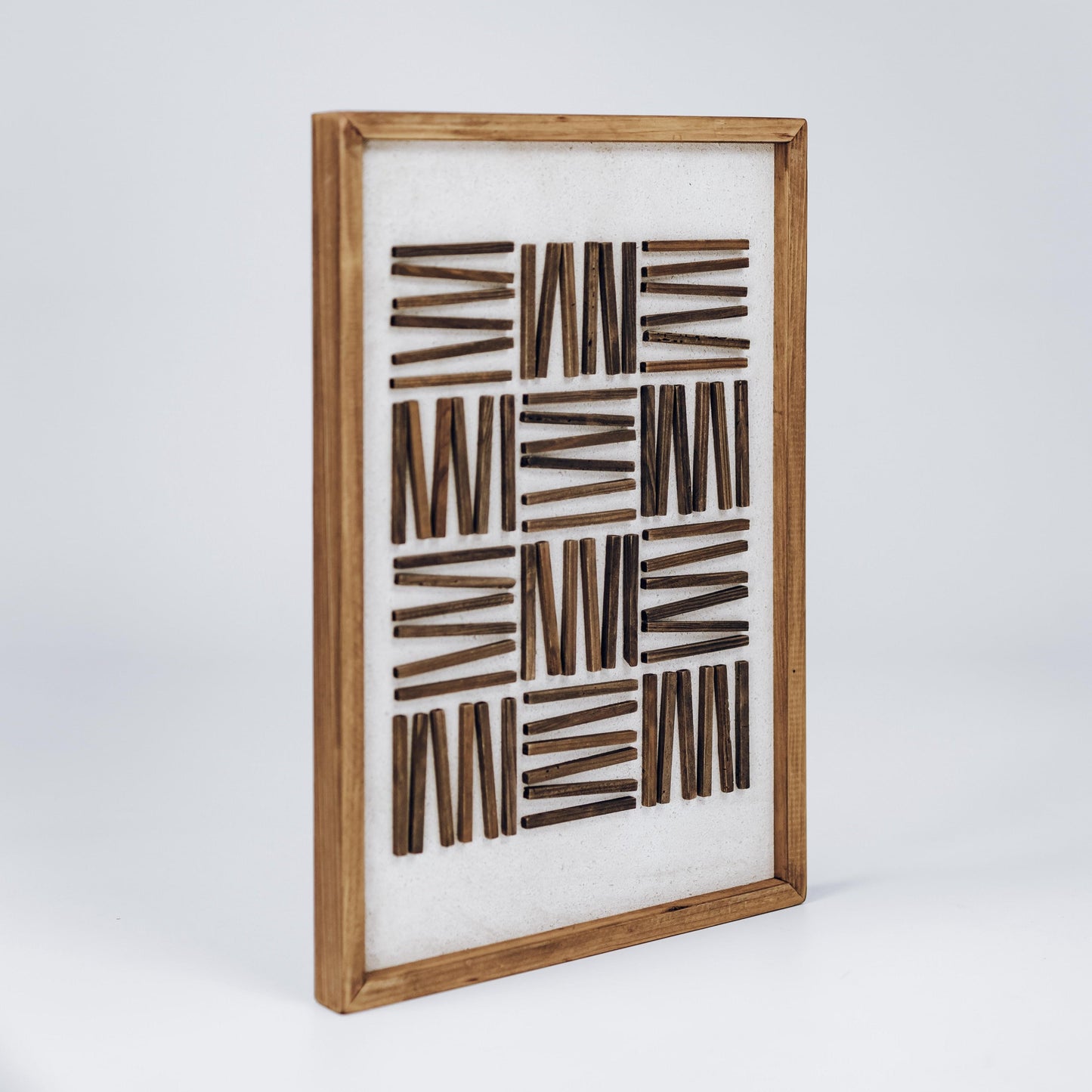 Framed abstract wall art with light wood frame and dark rectangular stripe pattern