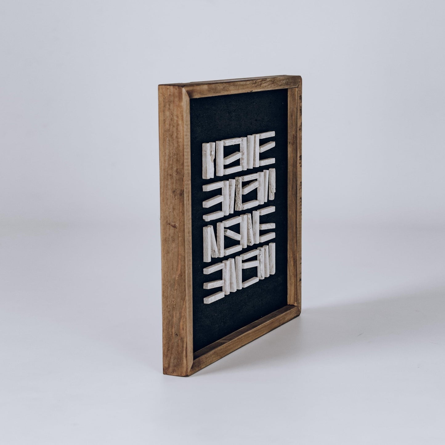 Freestanding framed wall art with dark backing, wooden frame, and white layered strip pattern.
