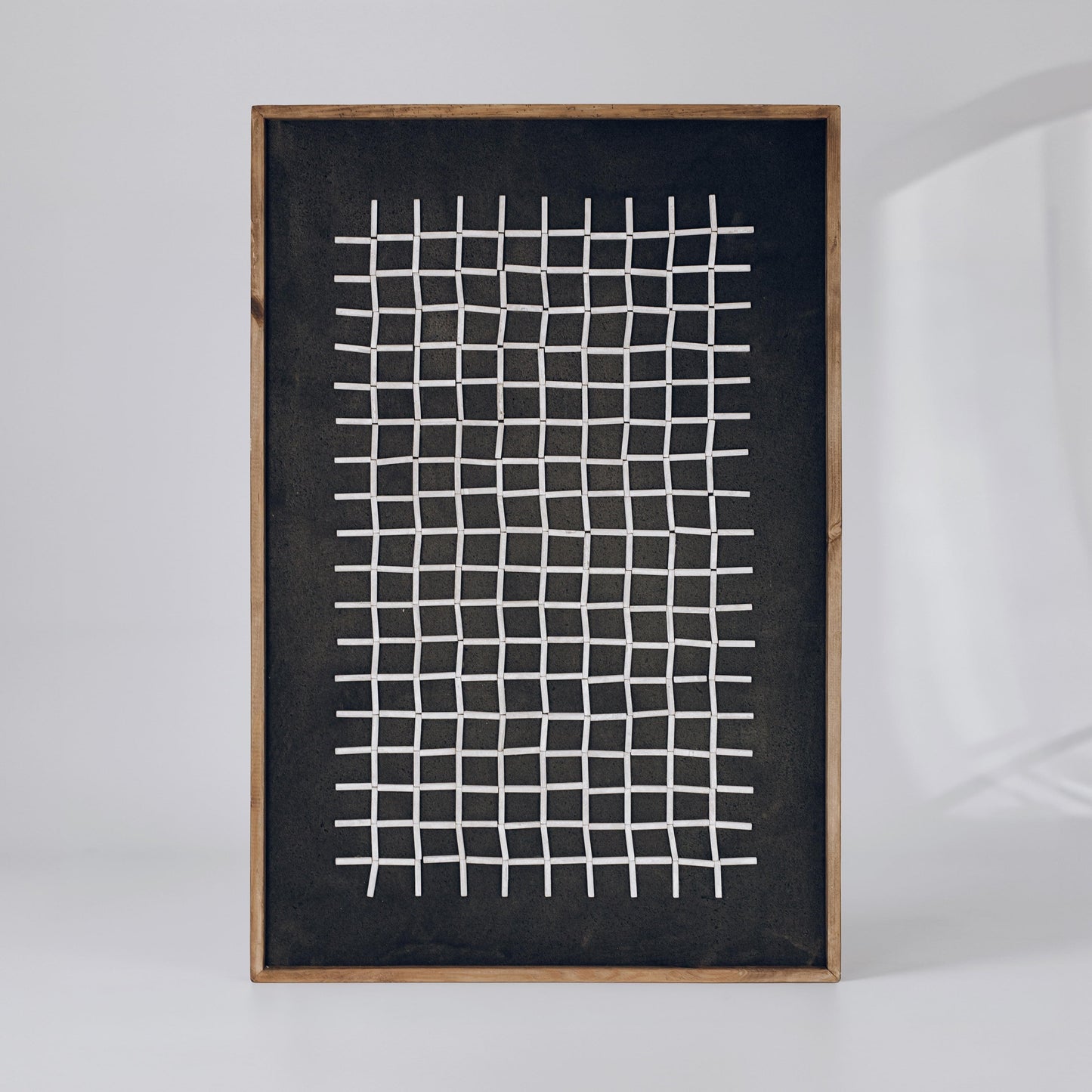 Framed dark wall art with wide white grid pattern on dark fabric background