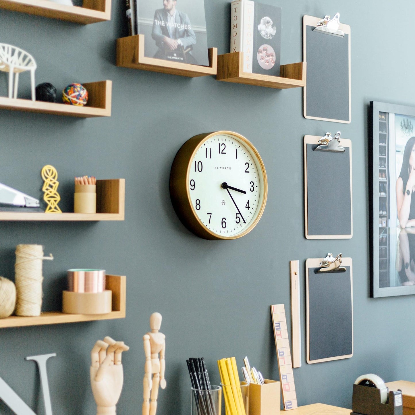Brass round wall clock on wall, white face with black numerals, black hands, Newgate logo.