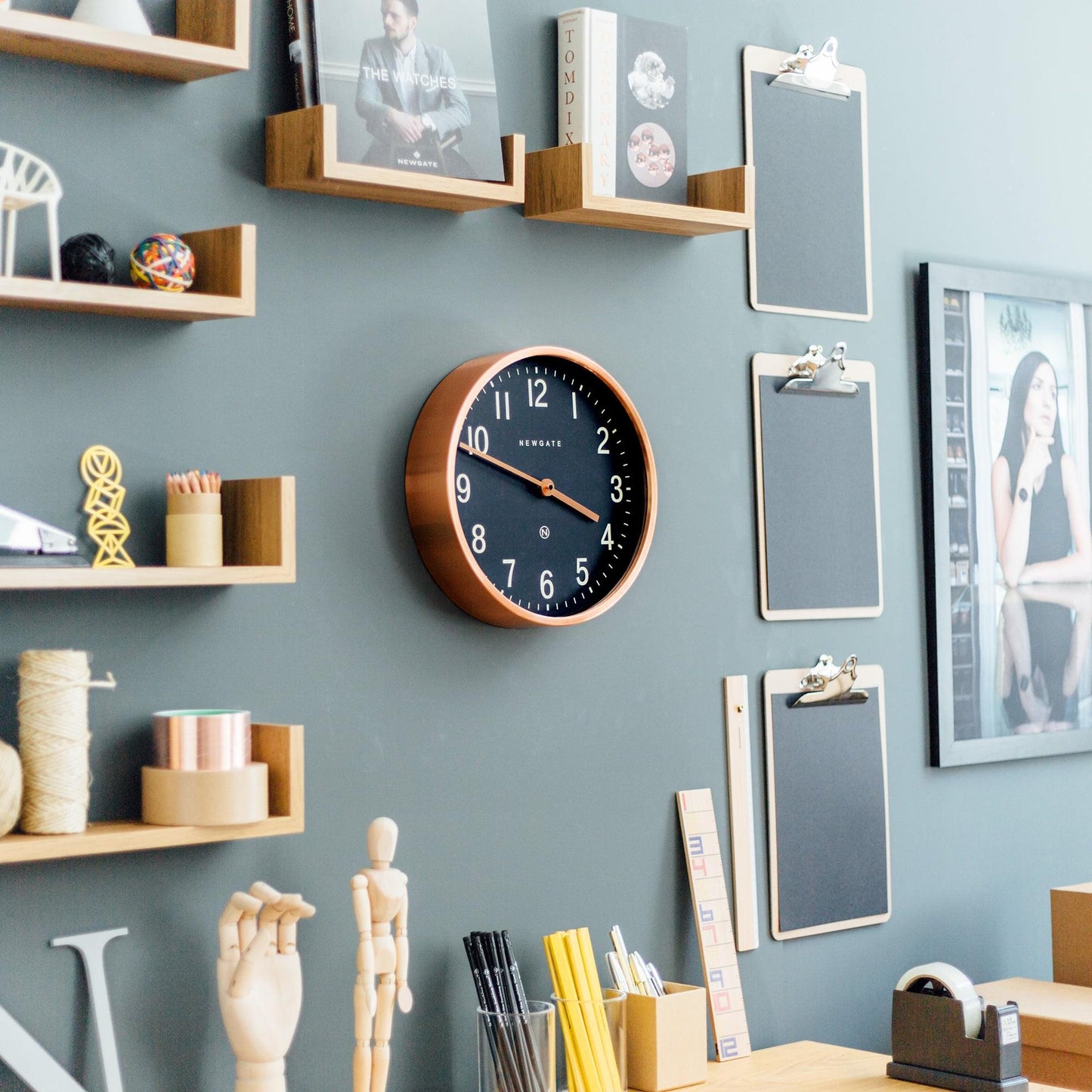 Copper-rim wall clock with dark blue dial on a home office wall near shelves