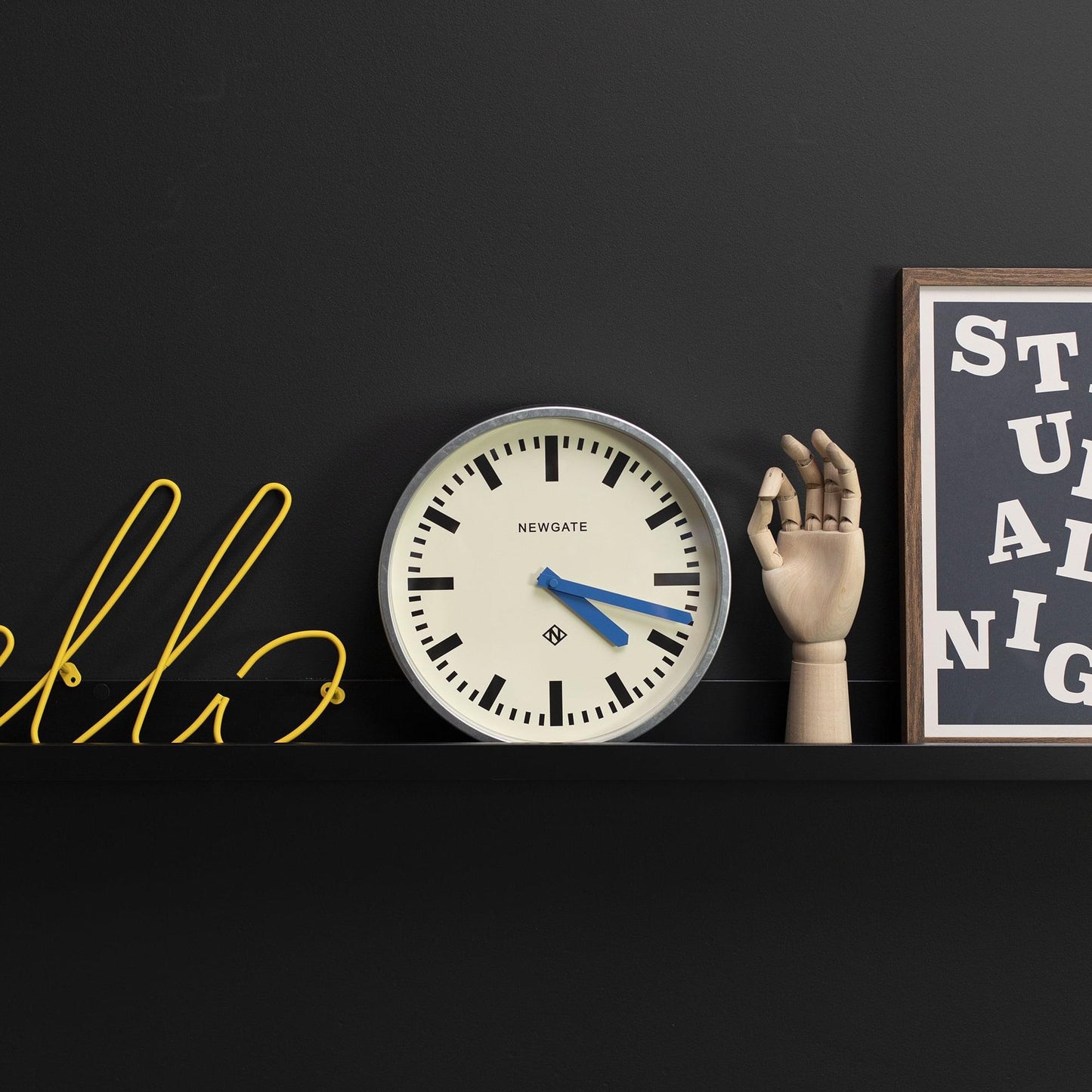 Wall clock on a shelf ledge, cream dial with blue hands and black minute markers