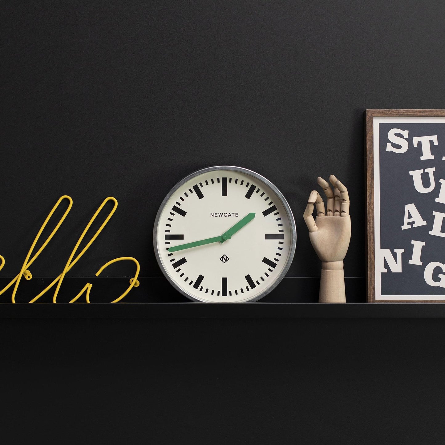 Wall clock with cream dial, black markers, green hands on a shelf