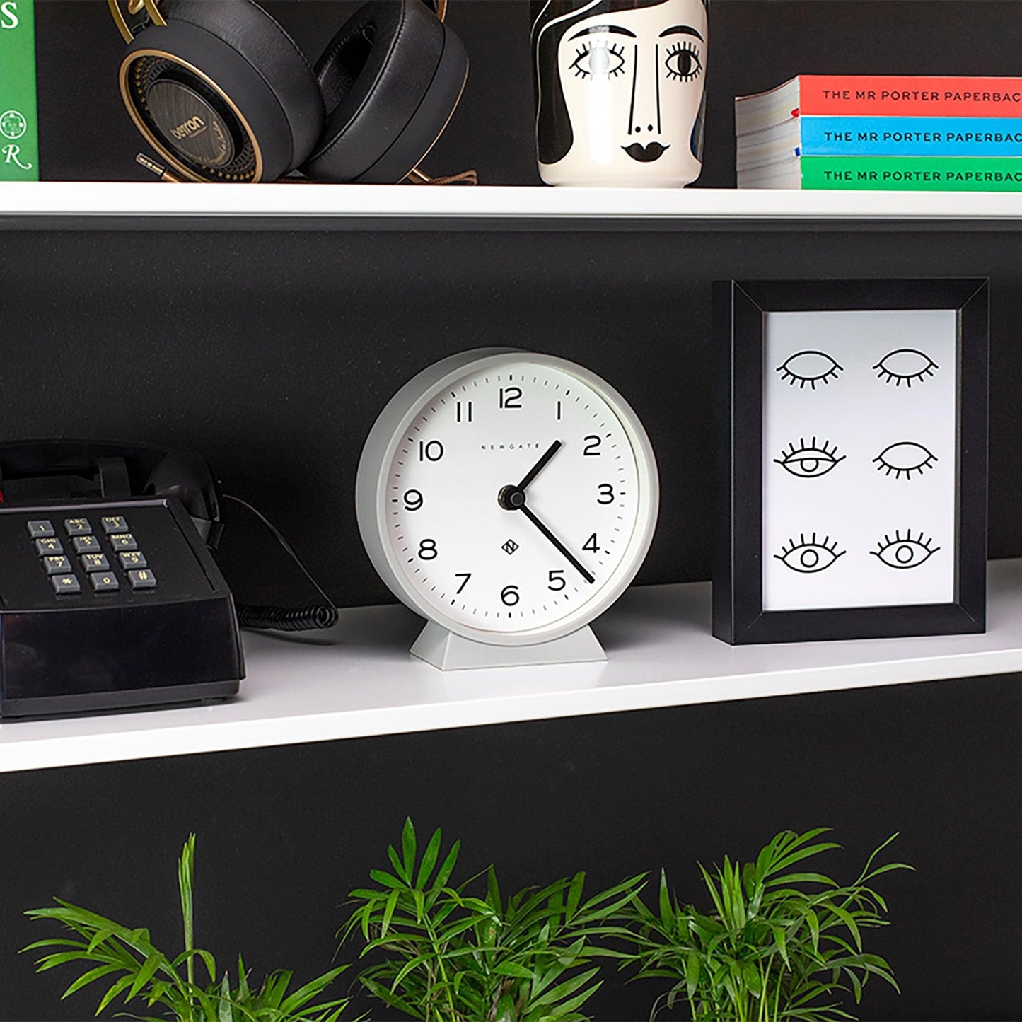 Grey mantel clock with white dial on a shelf
