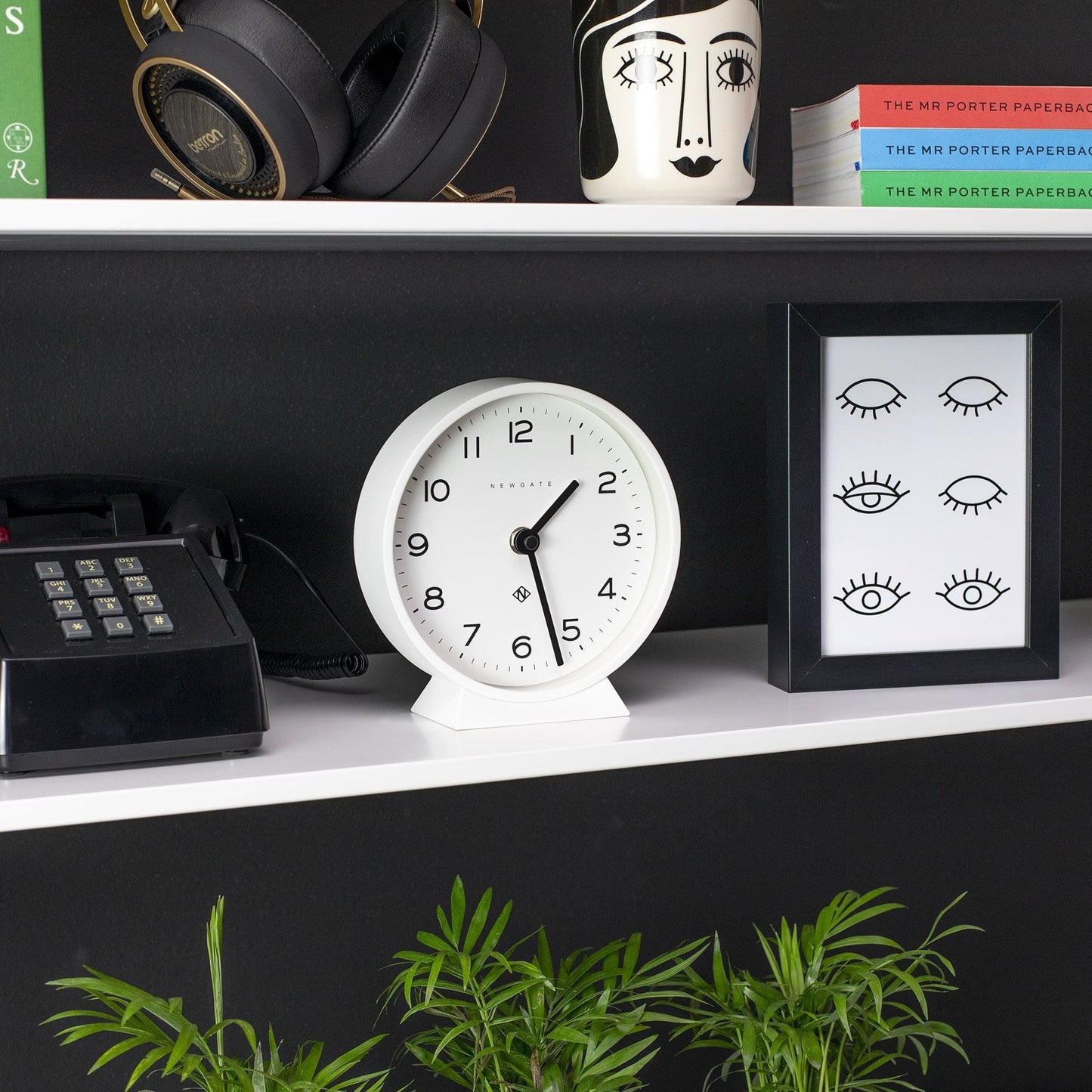 Pebble white mantel clock with black hands and numerals, set on a shelf.