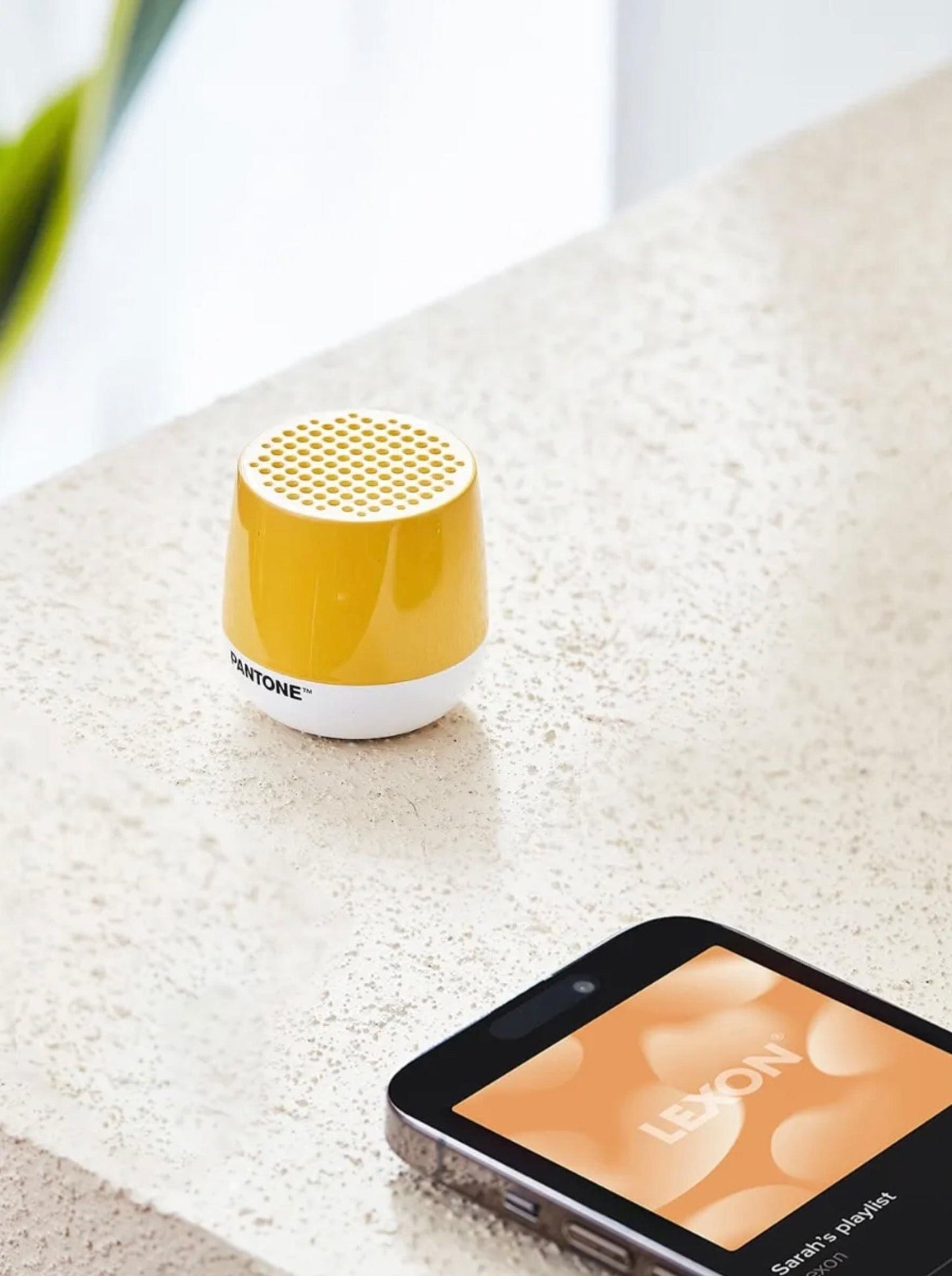 Yellow PANTONE mini Bluetooth speaker on light stone surface, perforated top grille
