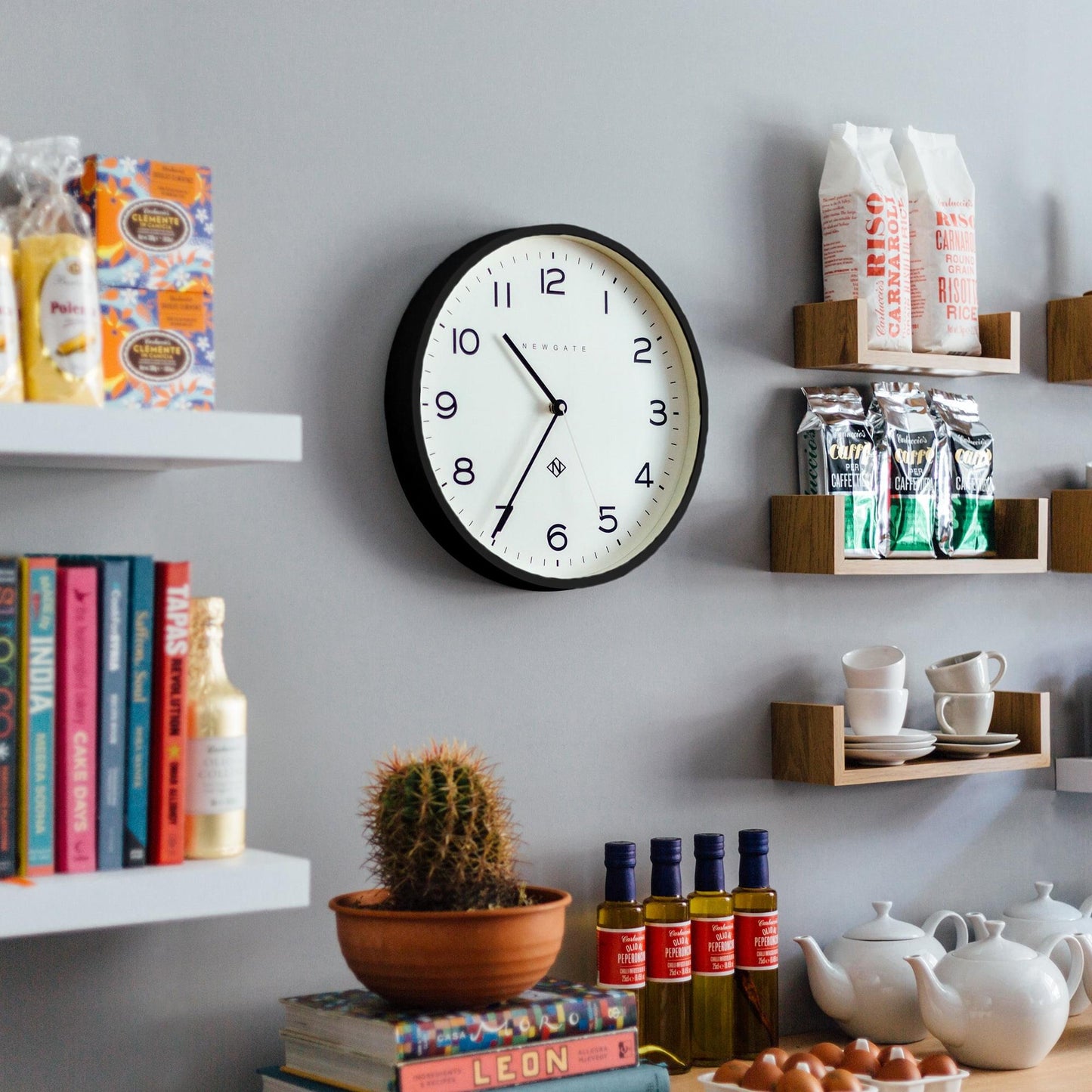 Black wall clock with white face and Arabic numerals, three hands shown