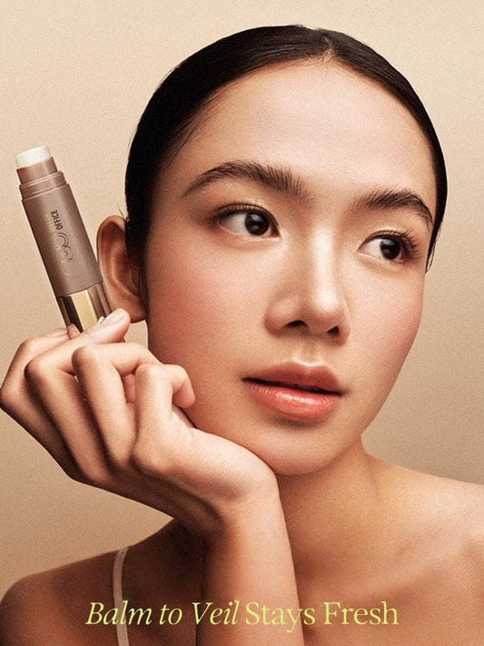 Makeup stick in cool taupe held near cheek with dome cap and gold logo