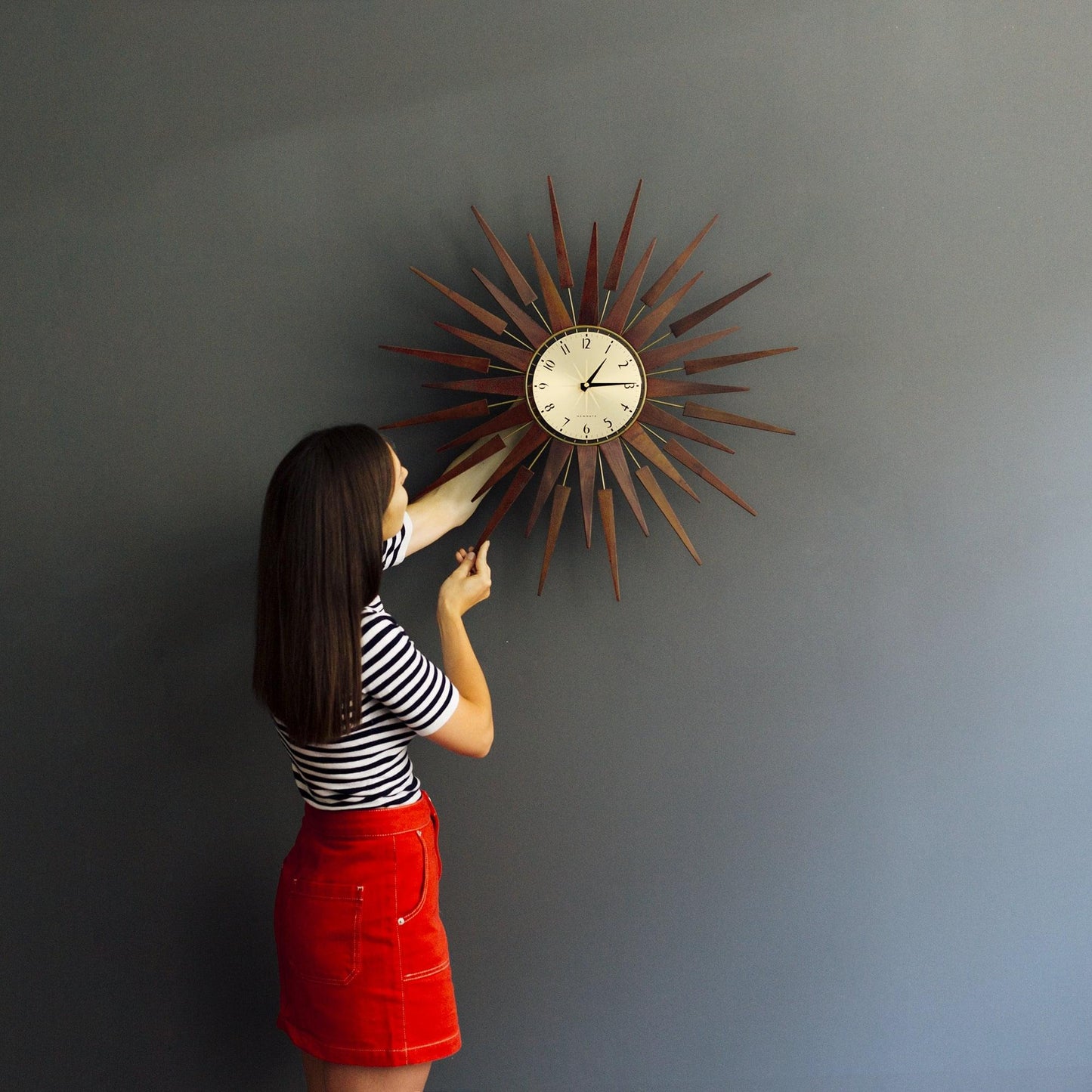 Newgate Pluto wall clock with cream dial and dark metal sunburst frame being adjusted