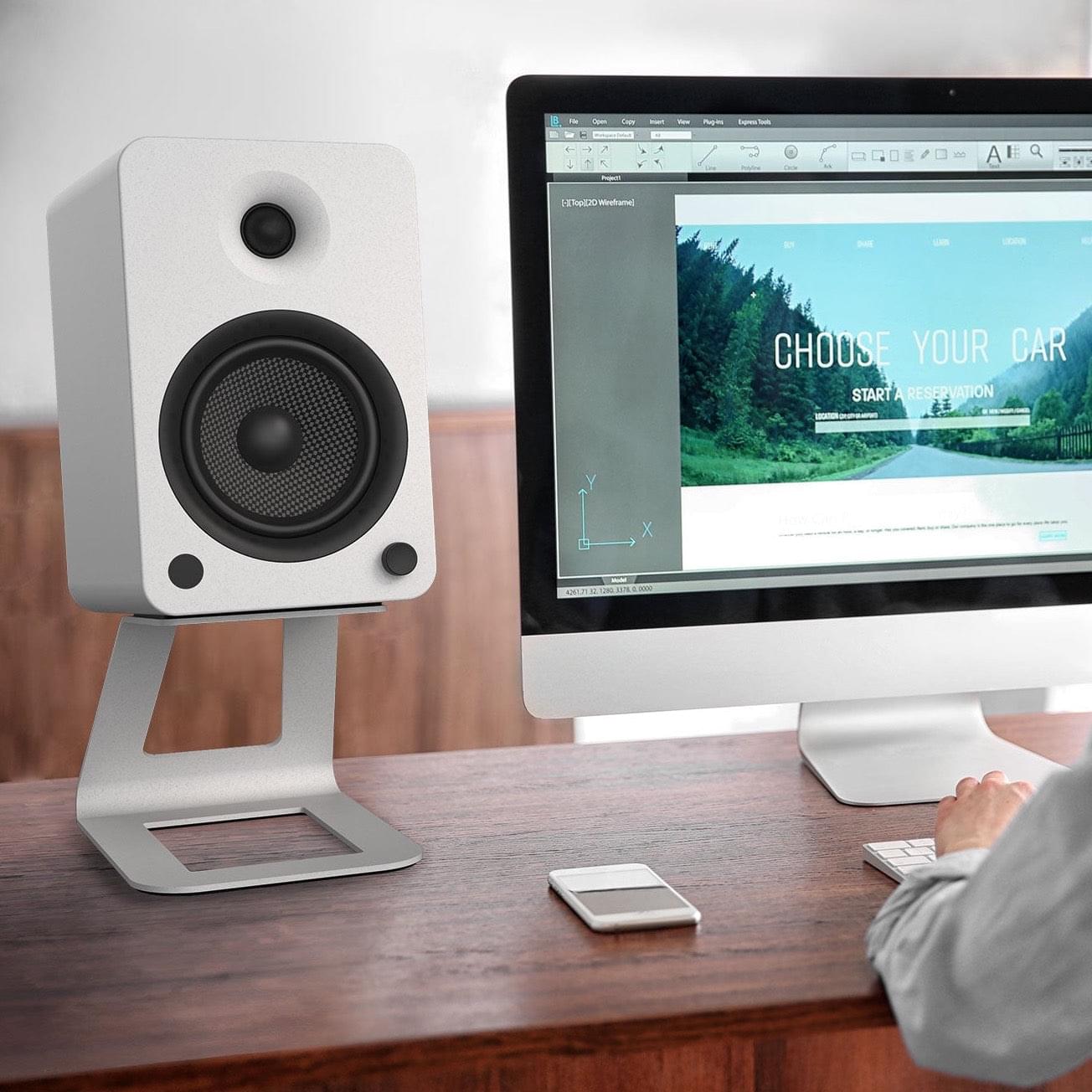 White elevated speaker stand holding a black speaker on a desktop