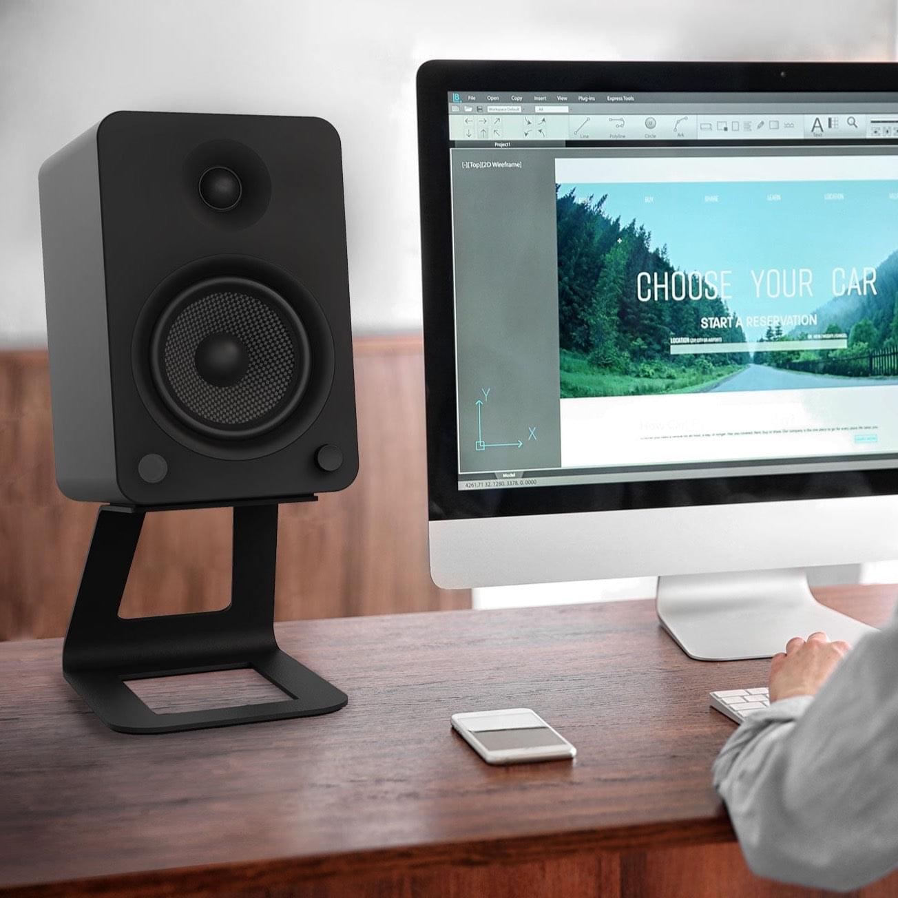 Black speaker stands holding studio monitor speakers on a desk