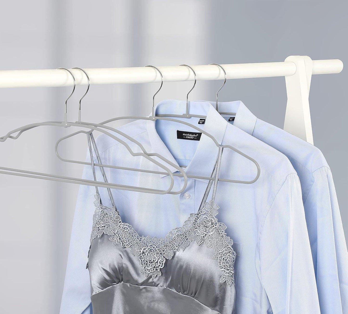 Grey metal hangers on a rod holding light blue shirts and a lace-trim camisole