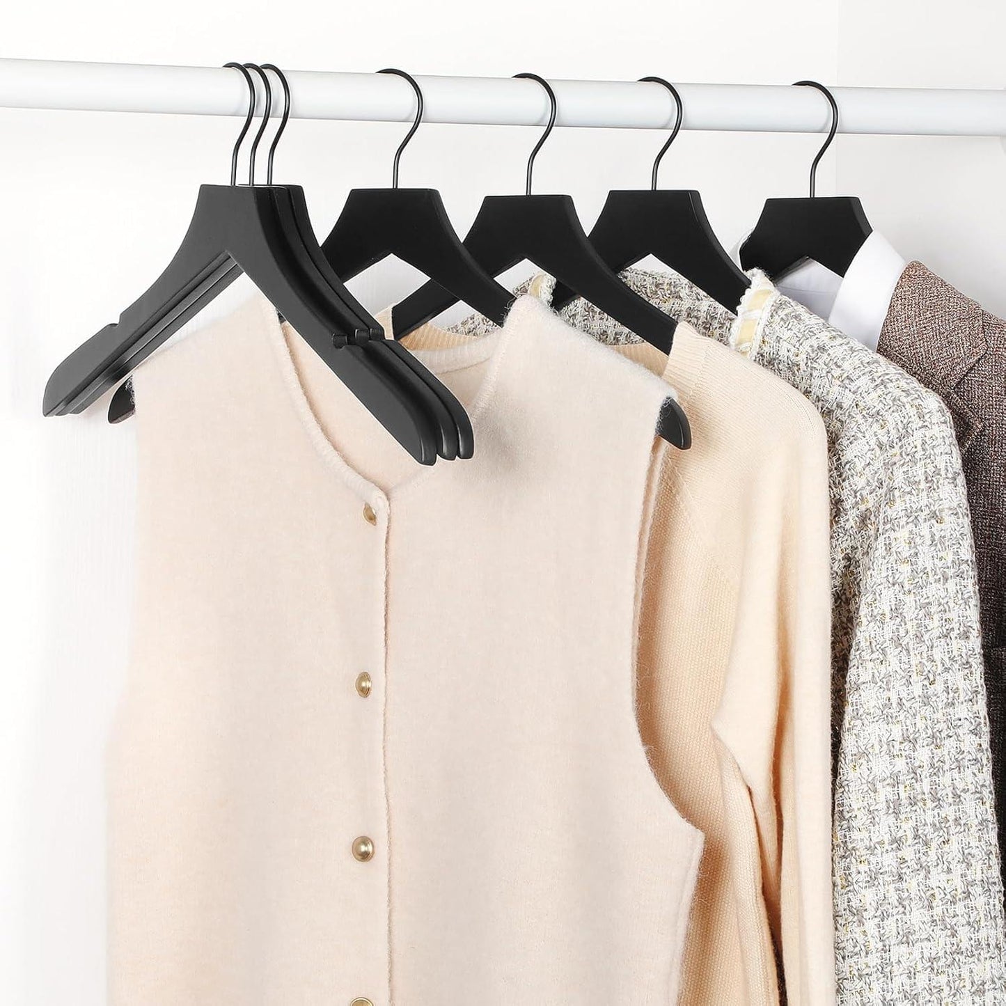 Black wooden hangers holding light-colored sweaters and a cream cardigan