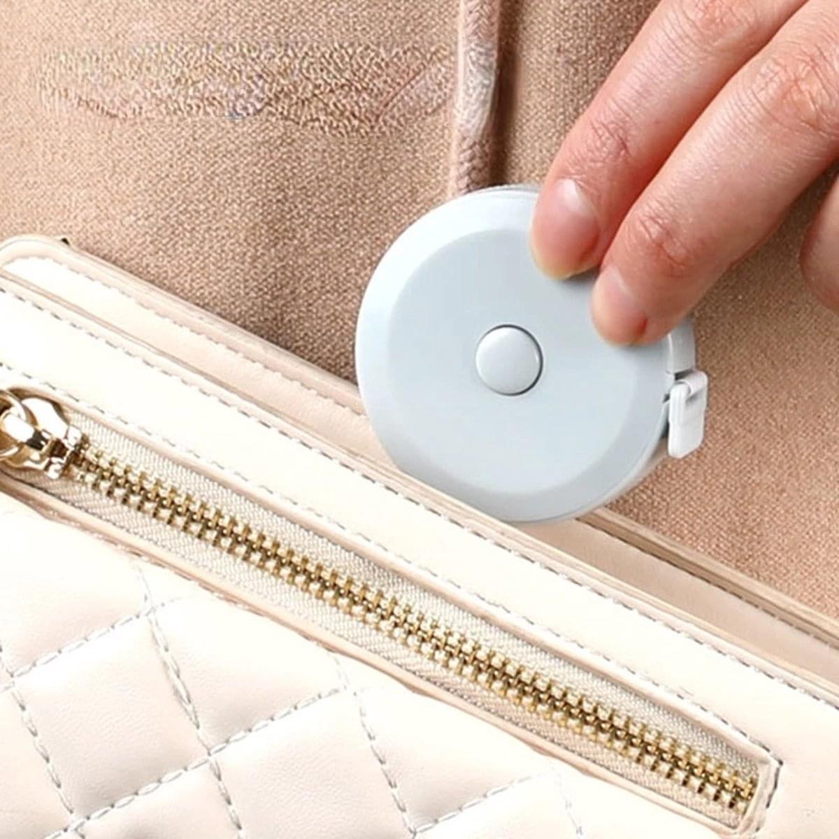 Round measuring tape clipped to a bag strap, with mint-green case and button