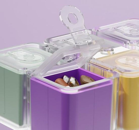 Clear-lidded pill organizer with open purple compartment holding small capsules