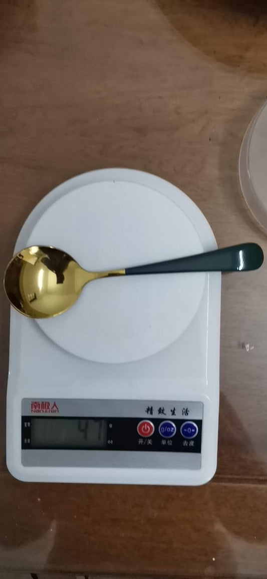Stainless steel spoon with gold bowl and blue handle on a kitchen scale.