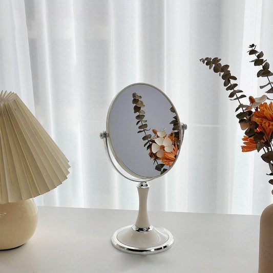 Round tabletop makeup mirror with chrome stand and reflective center surface on desk
