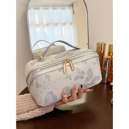 Portable toiletry bag with cream floral pattern, dual gold-tone zippers, top handle