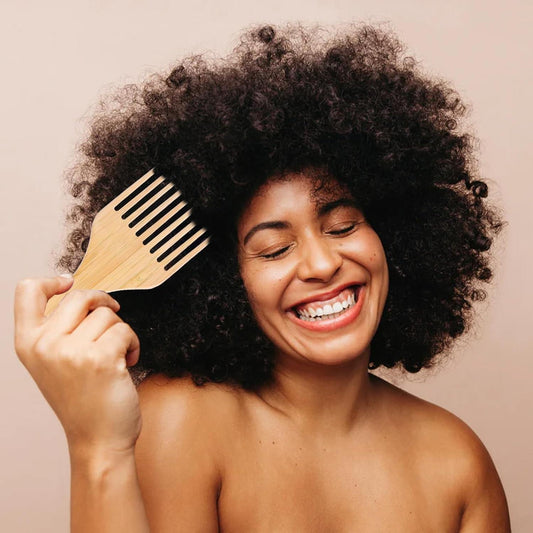 Wide-tooth wooden comb with pick, held near curly hair for detangling