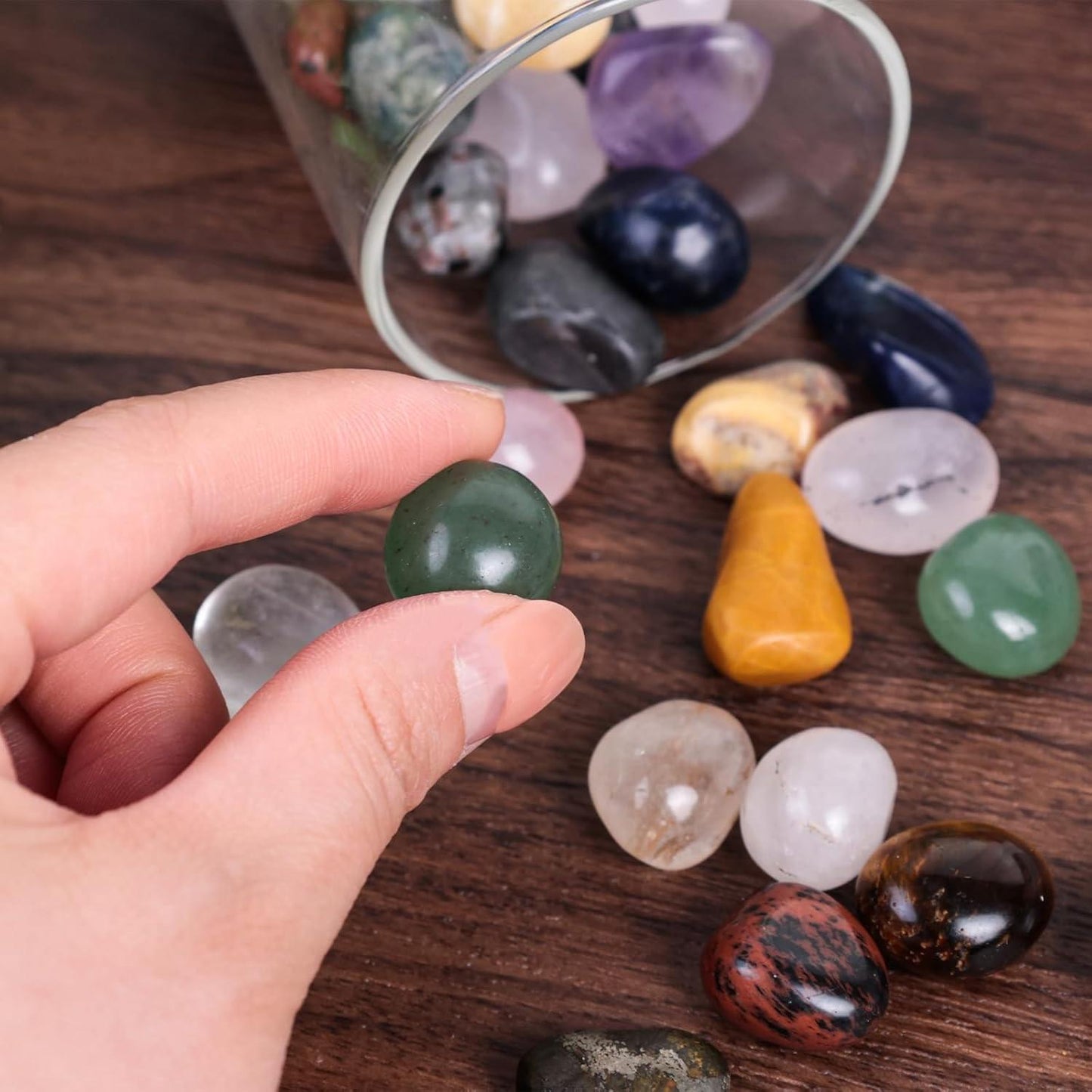 Hand holding tumbled gemstone chips, smooth oval stones in green, pink, and amber tones