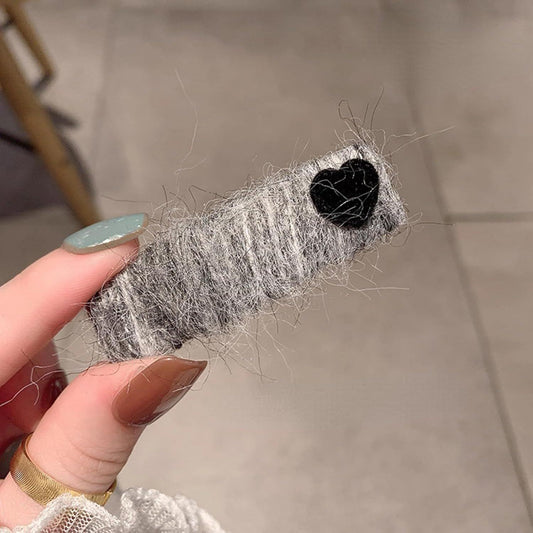 Gray fuzzy heart hair clip held in hand with black velvet hearts