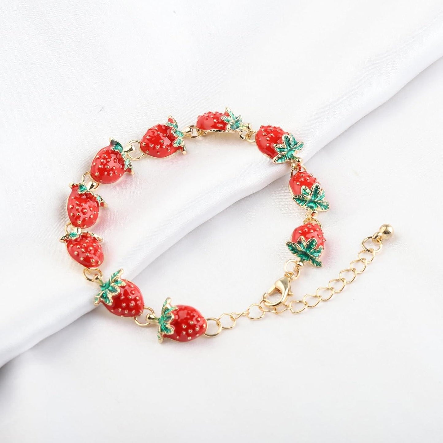 Strawberry charm bracelet with red strawberry beads and green leaf charms on white cloth