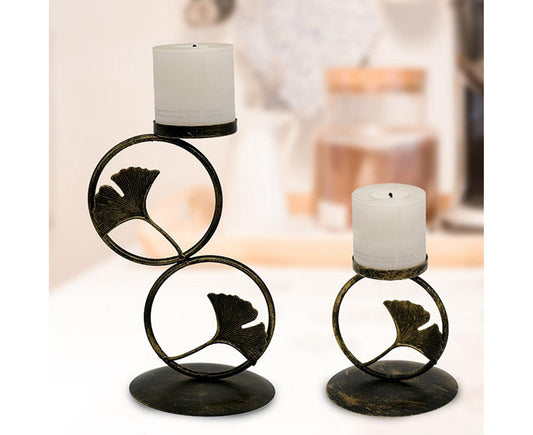 Gold-tone ring candlestick holders with leaf cutout, dark circular bases and white candles
